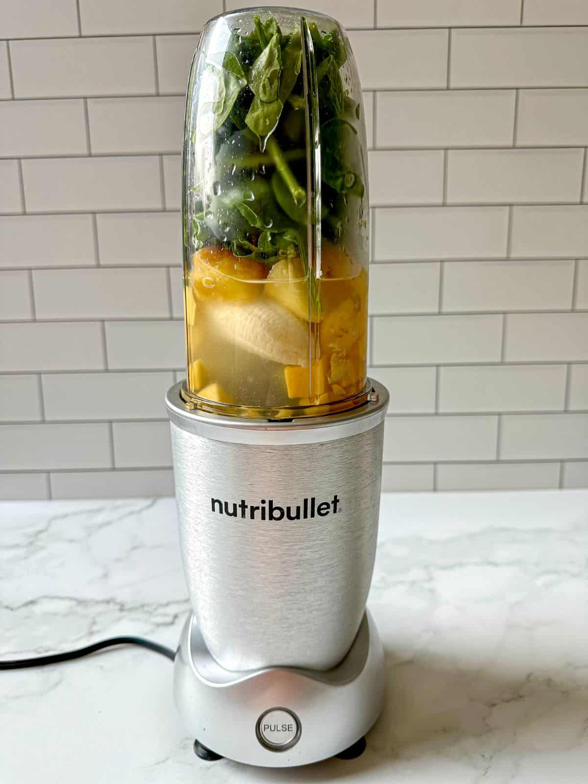 Spinach, banana, mango, pineapple, ginger, and coconut water are in a blender.