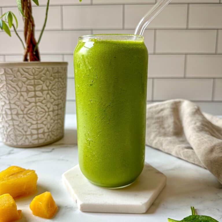A green smoothie in a glass with tropical fruit surrounding the drink.