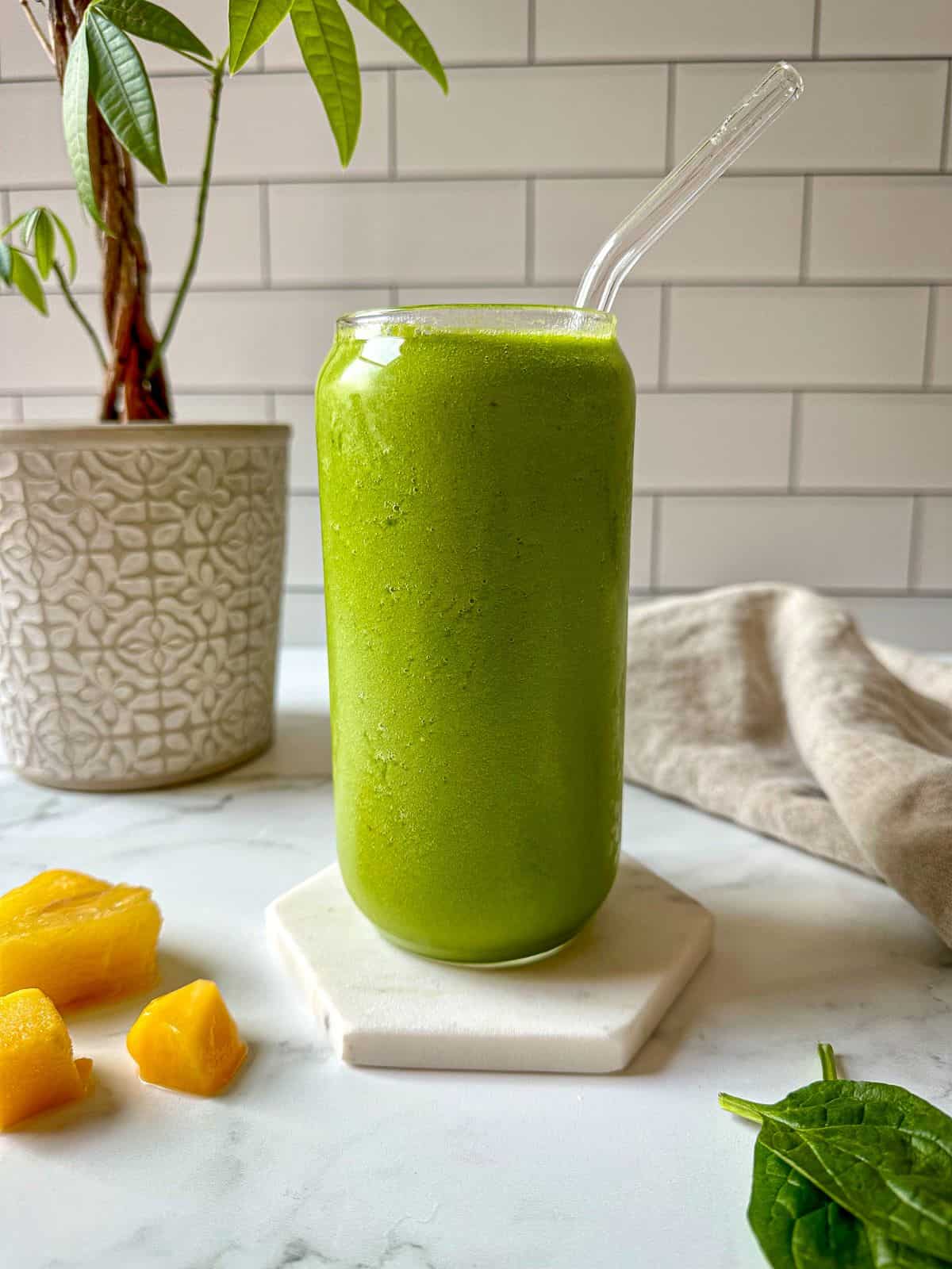 A green smoothie in a glass with tropical fruit surrounding the drink.