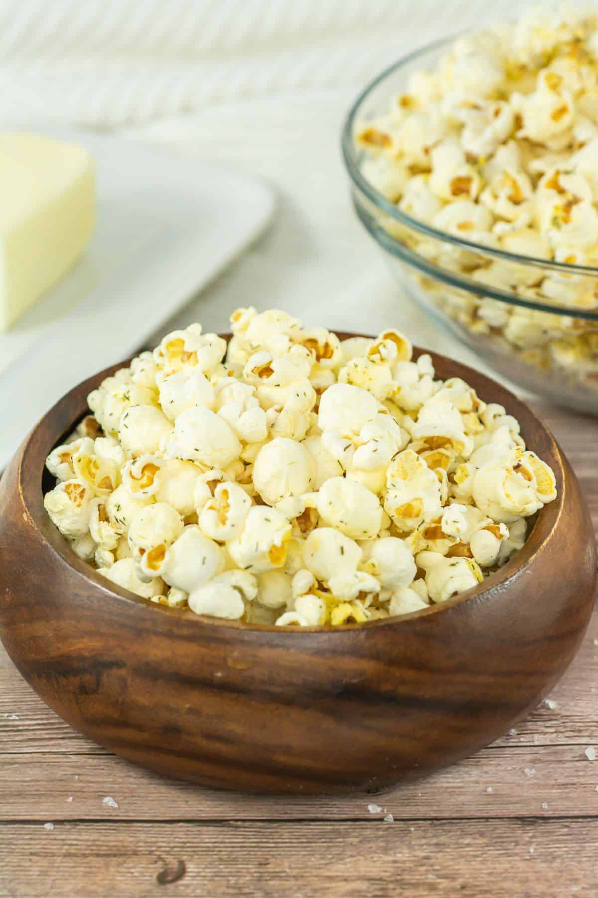 A wooden bowl filled with salt and vinegar popcorn with a stick of butter behind it.