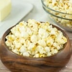 A wooden bowl filled with salt and vinegar popcorn with a stick of butter behind it.