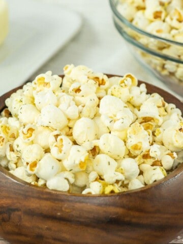 A wooden bowl filled with salt and vinegar popcorn with a stick of butter behind it.