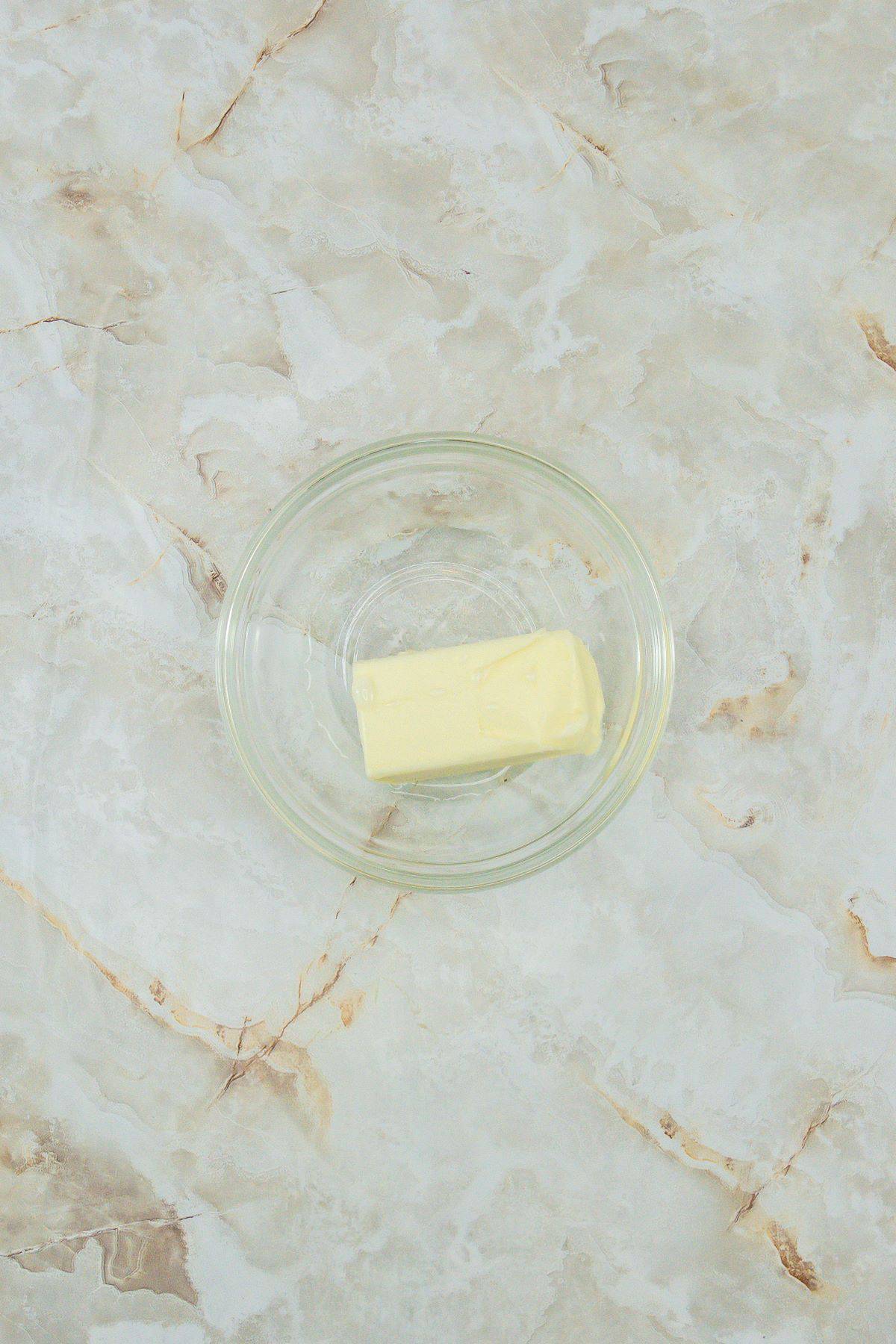 A stick of butter and white vinegar in a small bowl.