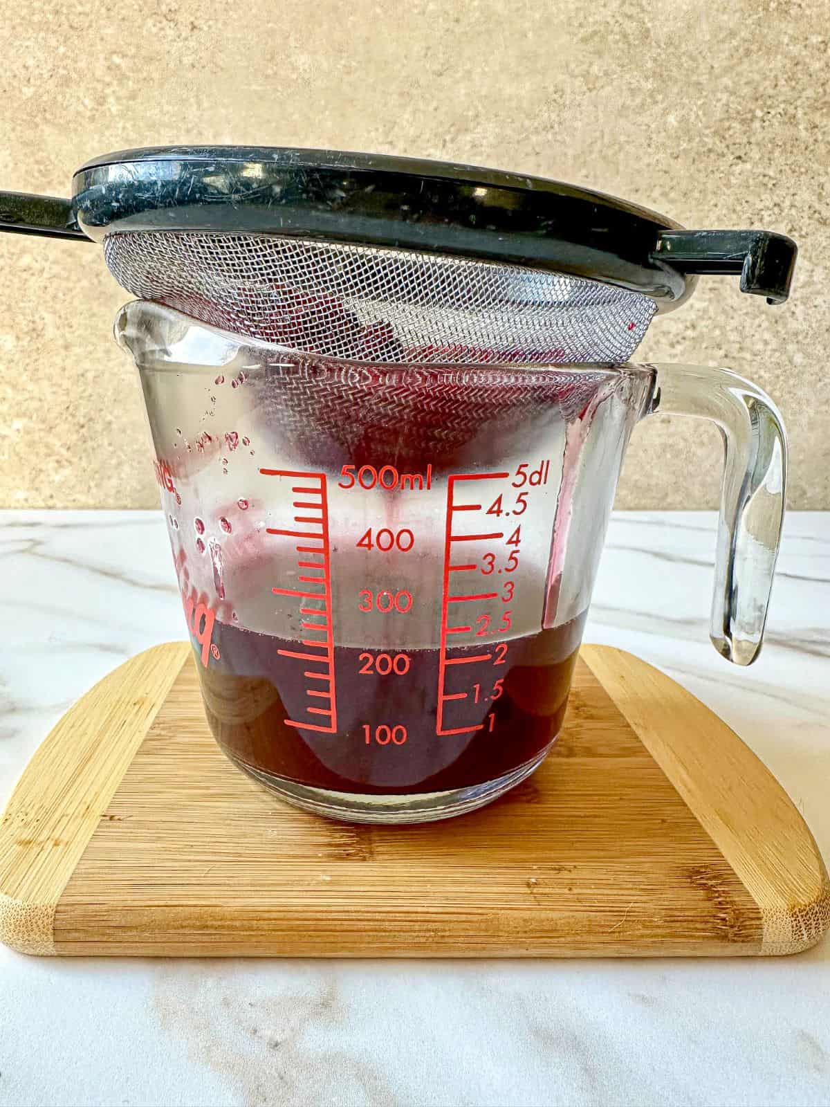 Blackberry simple syrup strained into a glass measuring cup using a mesh sieve.