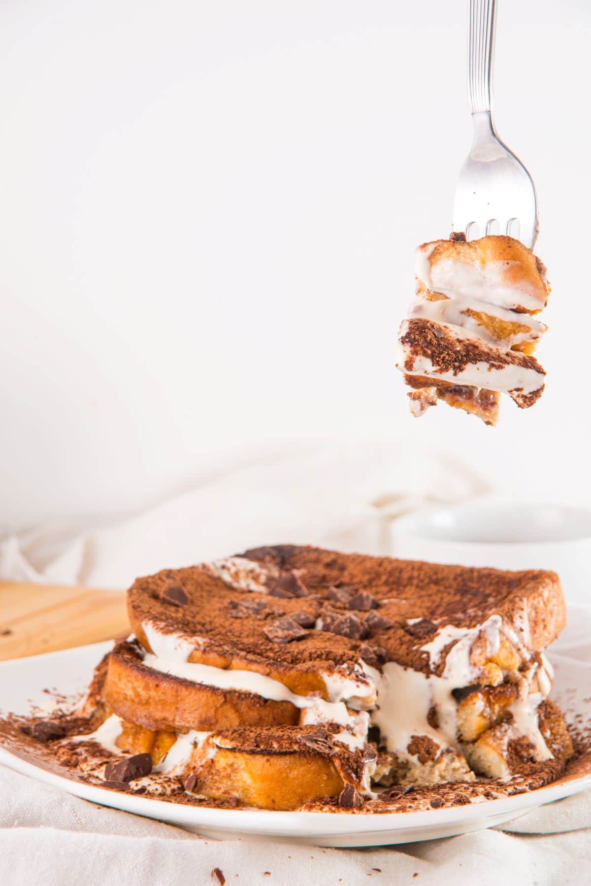 A fork grabbing a bite of creamy tiramisu French toast with mascarpone whipped cream.