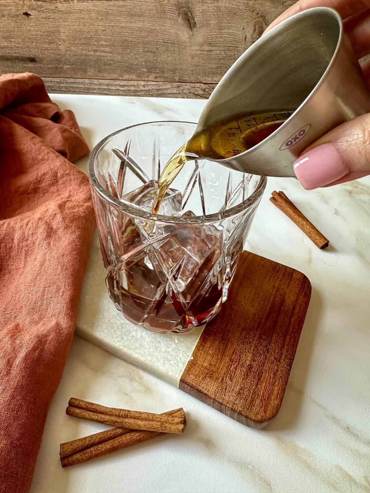 A hand pouring a jigger of bourbon into a rocks glass.