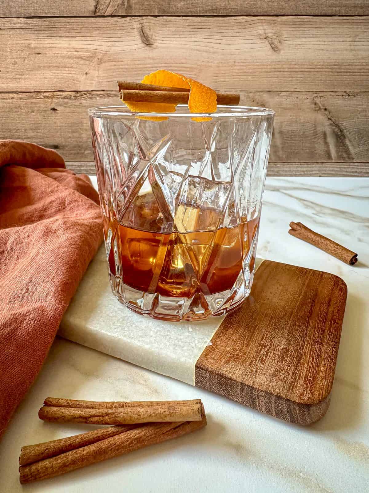 A cinnamon old fashioned in a rock glass garnished with an orange peel and cinnamon stick.