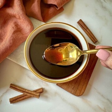 A brown cinnamon simple syrup in a bowl with a golden spoon.