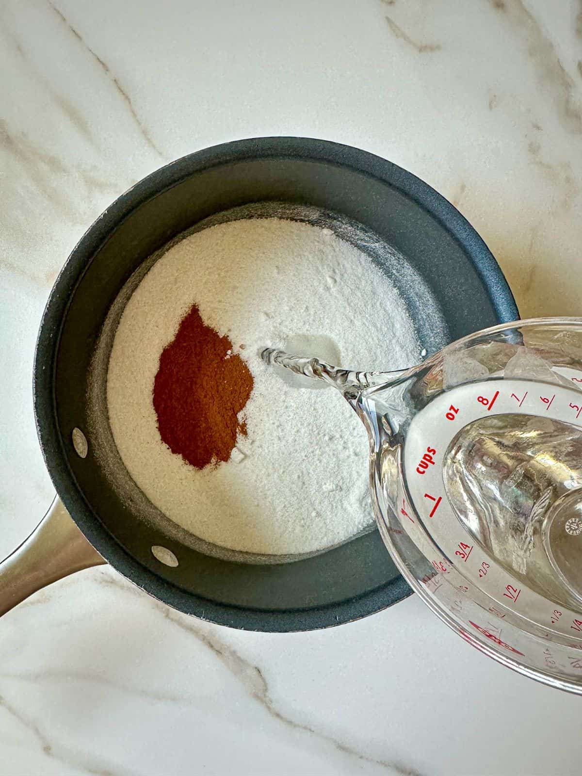 Cinnamon and sugar in a saucepan with water being poured in.