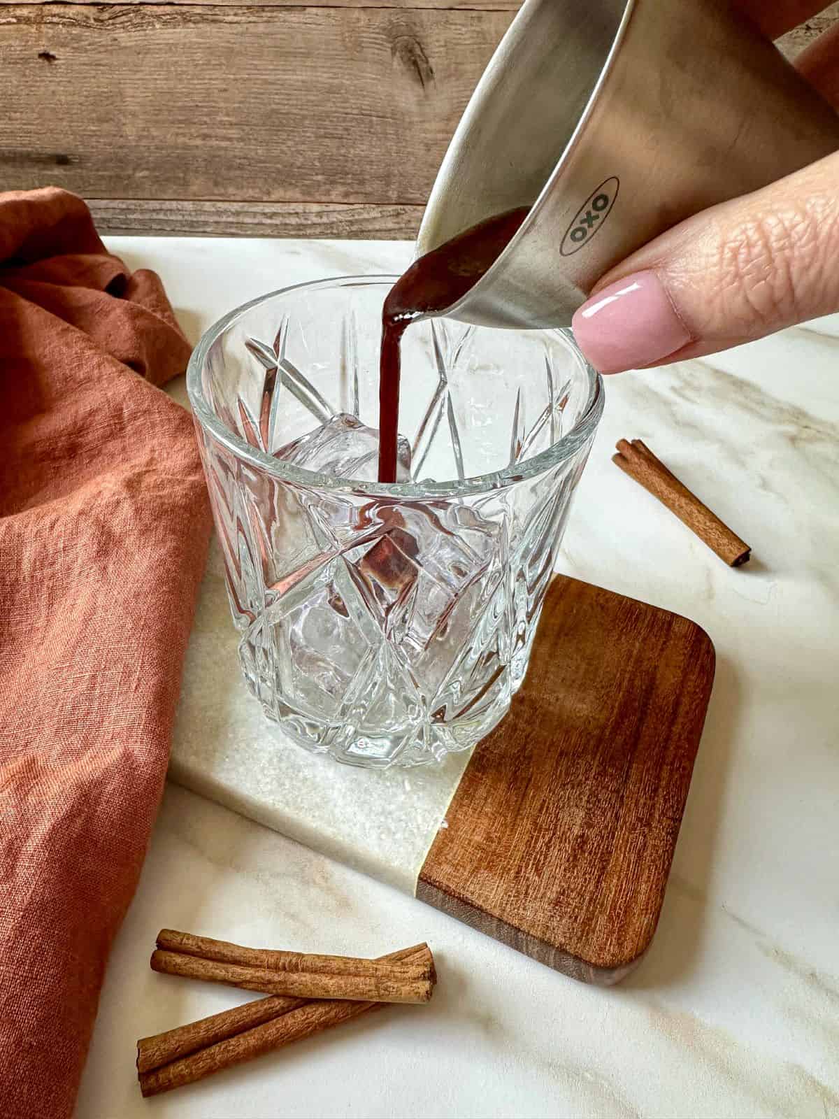 A hand pouring cinnamon simple syrup into a rocks glass with ice.