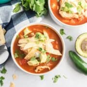 Two bowls of tortilla soup with tortilla stripes and avocado on top.