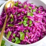 Red cabbage slaw, an easy side or shrimp taco topping, in a bowl with spoon and chopped cilantro.