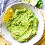 Guacamole, a classic side for shrimp tacos, in a large bowl with a tortilla chip.