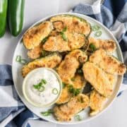 Jalapeno poppers on a serving platter with a small bowl of dipping sauce.