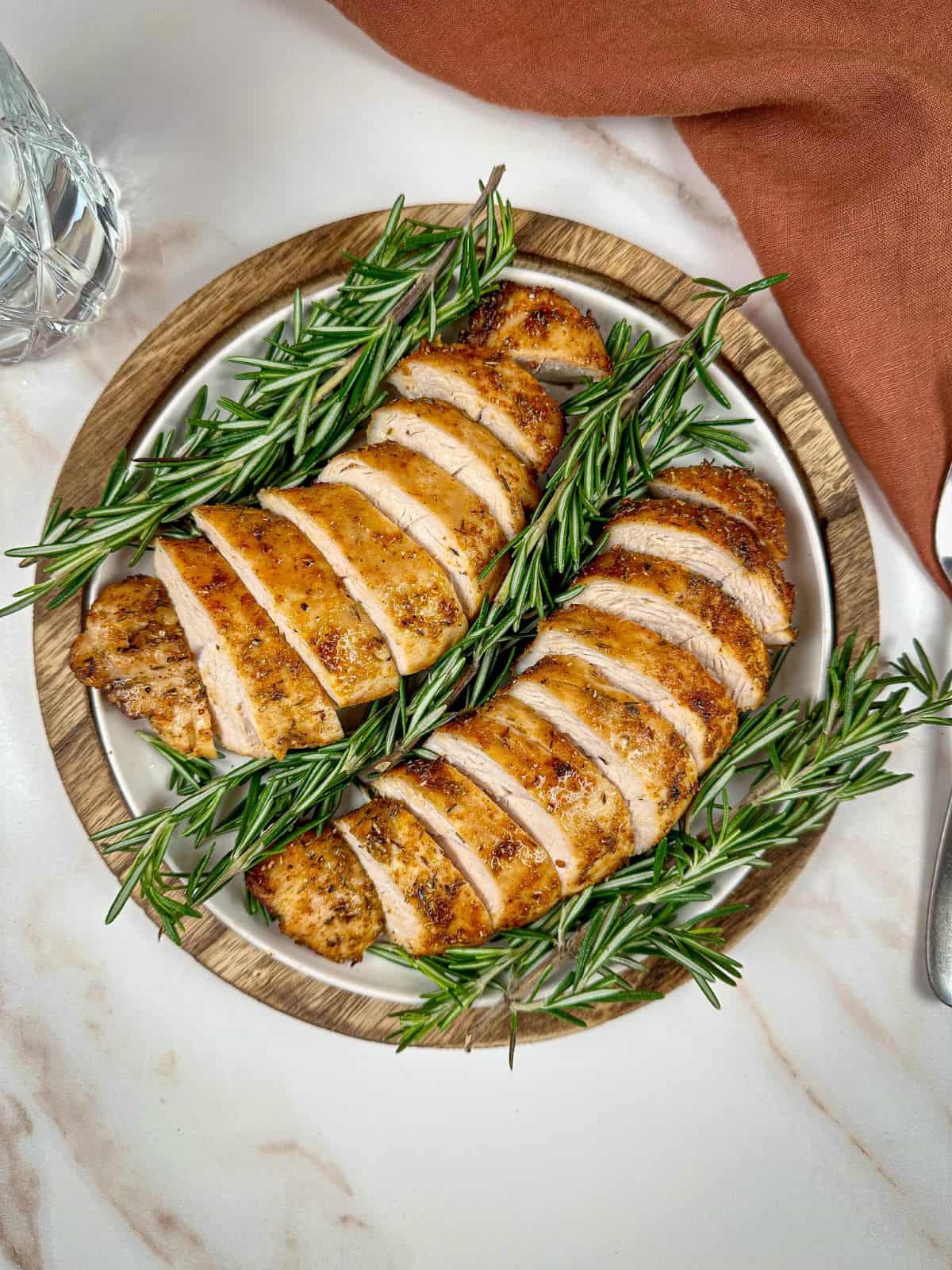 Air fryer boneless turkey breast tenderloin on a white plate with rosemary.