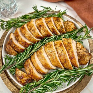 Air fryer turkey tenderloin on a plate sliced into medallions with a rosemary garnish.