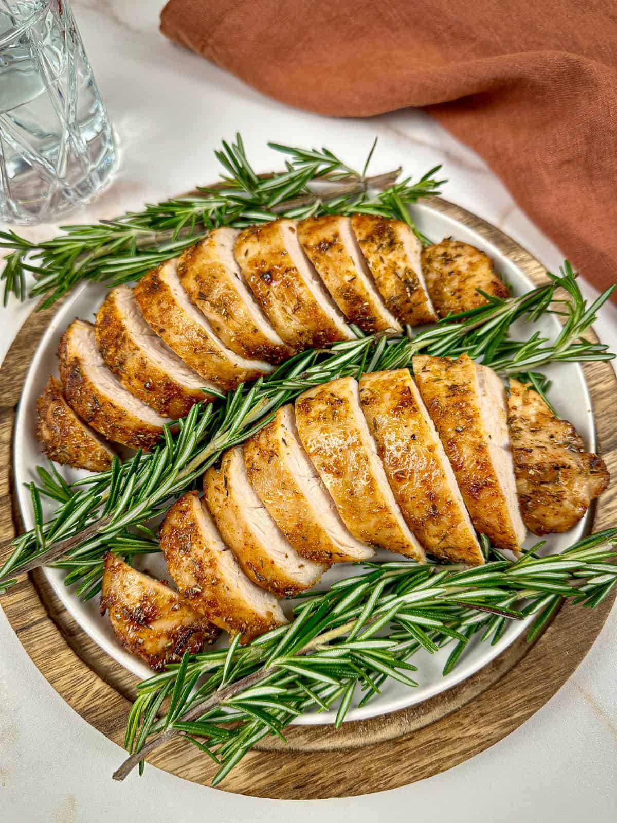 Air fryer turkey tenderloin on a plate sliced into medallions with a rosemary garnish. 