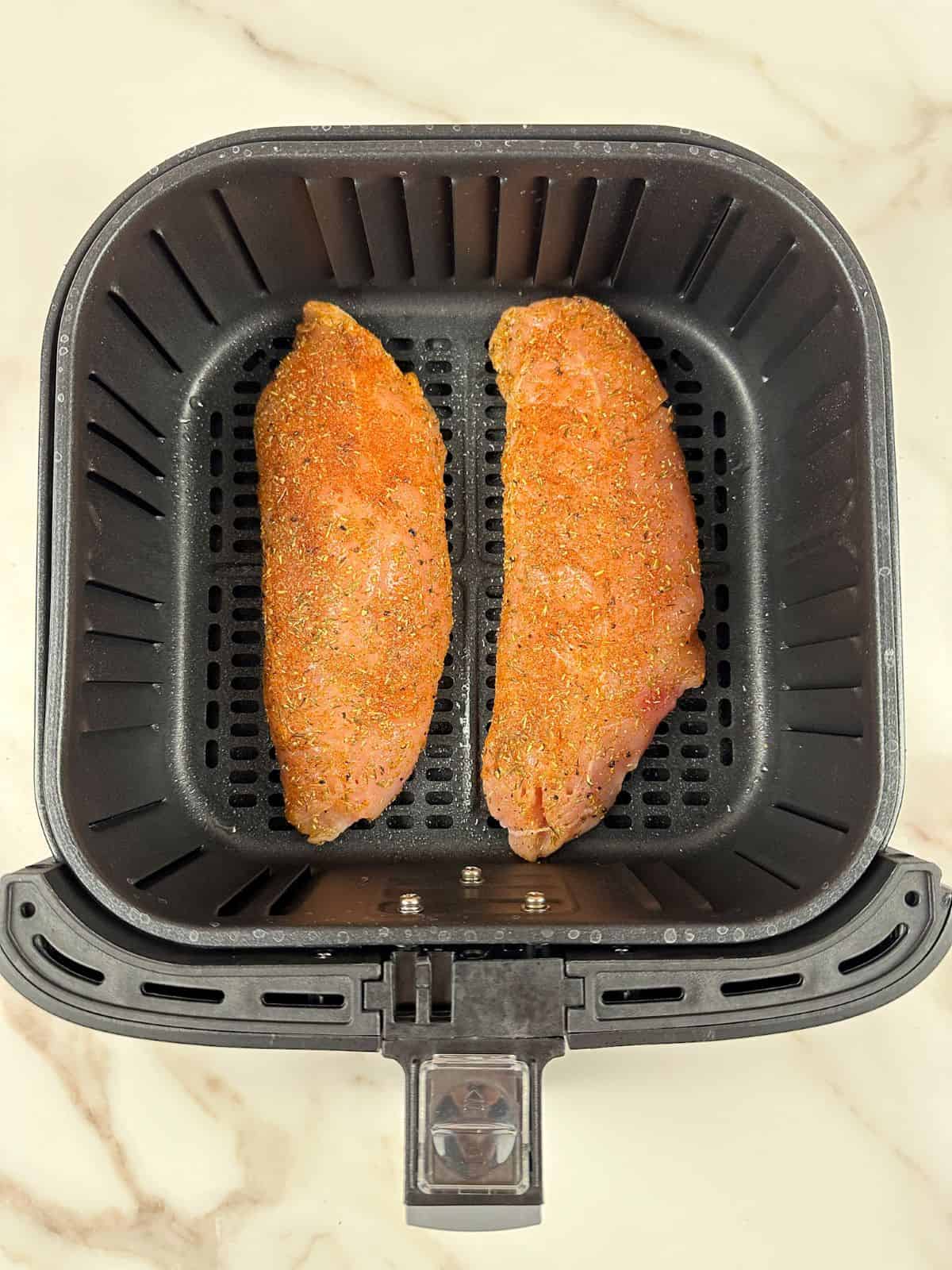 Two raw turkey tenderloins in air fryer basket.