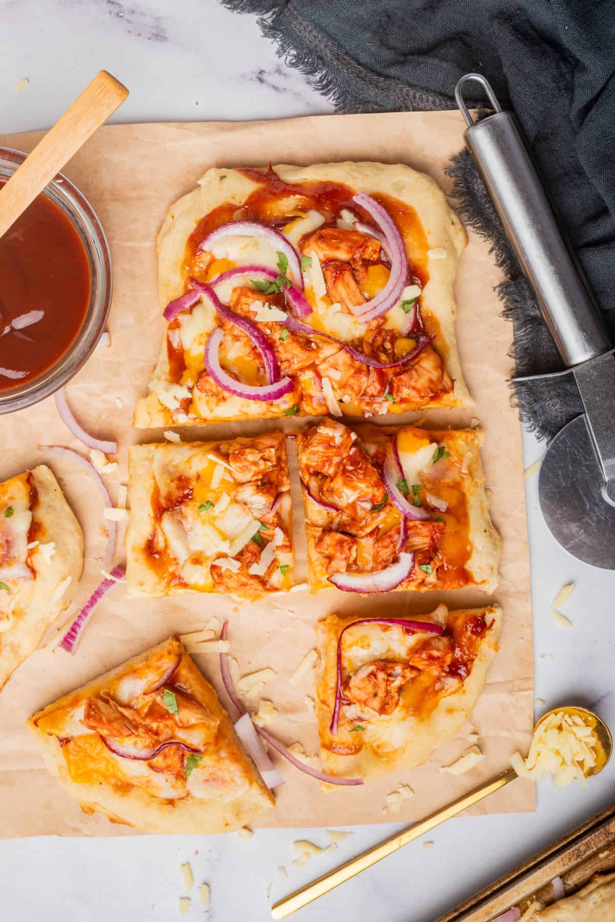 BBQ chicken flatbread pizza on a cutting board sliced into six square pieces.