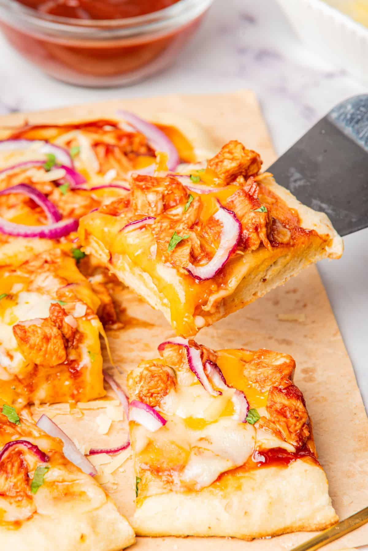 A square slice of bbq chicken flatbread pizza getting picked up with a spatula showing melted cheese.