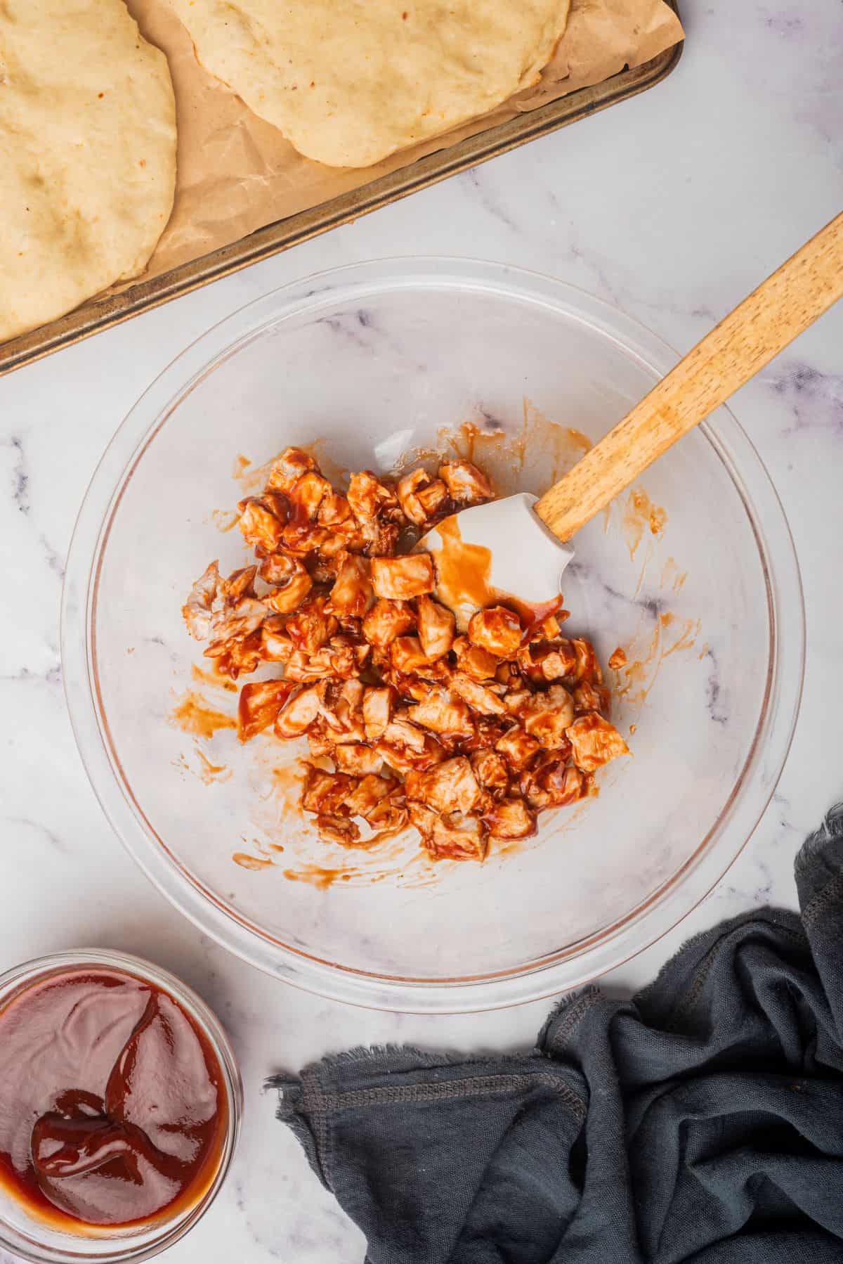 In a large glass bowl, chopped chicken is getting tossed in bbq sauce.