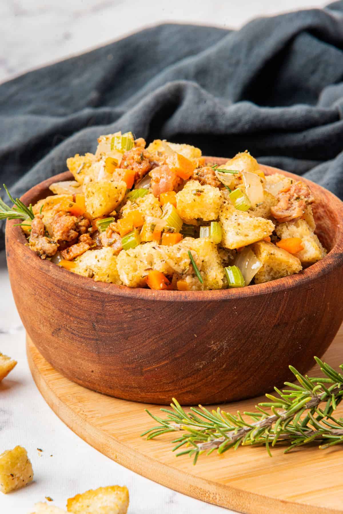 A wooden serving bowl filled with stovetop sausage stuffing is on a table.