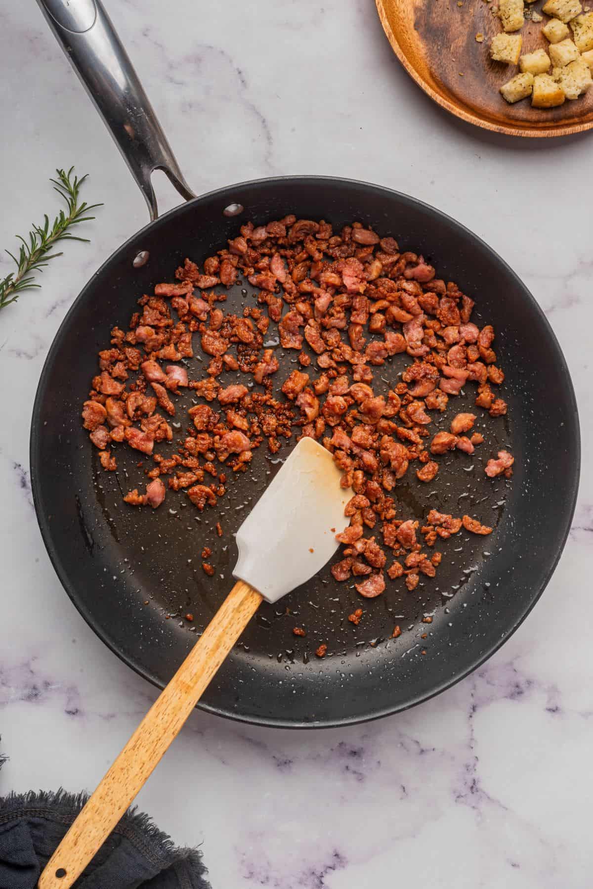 Browned ground sausage in a skillet with a spatula stirring the meat.