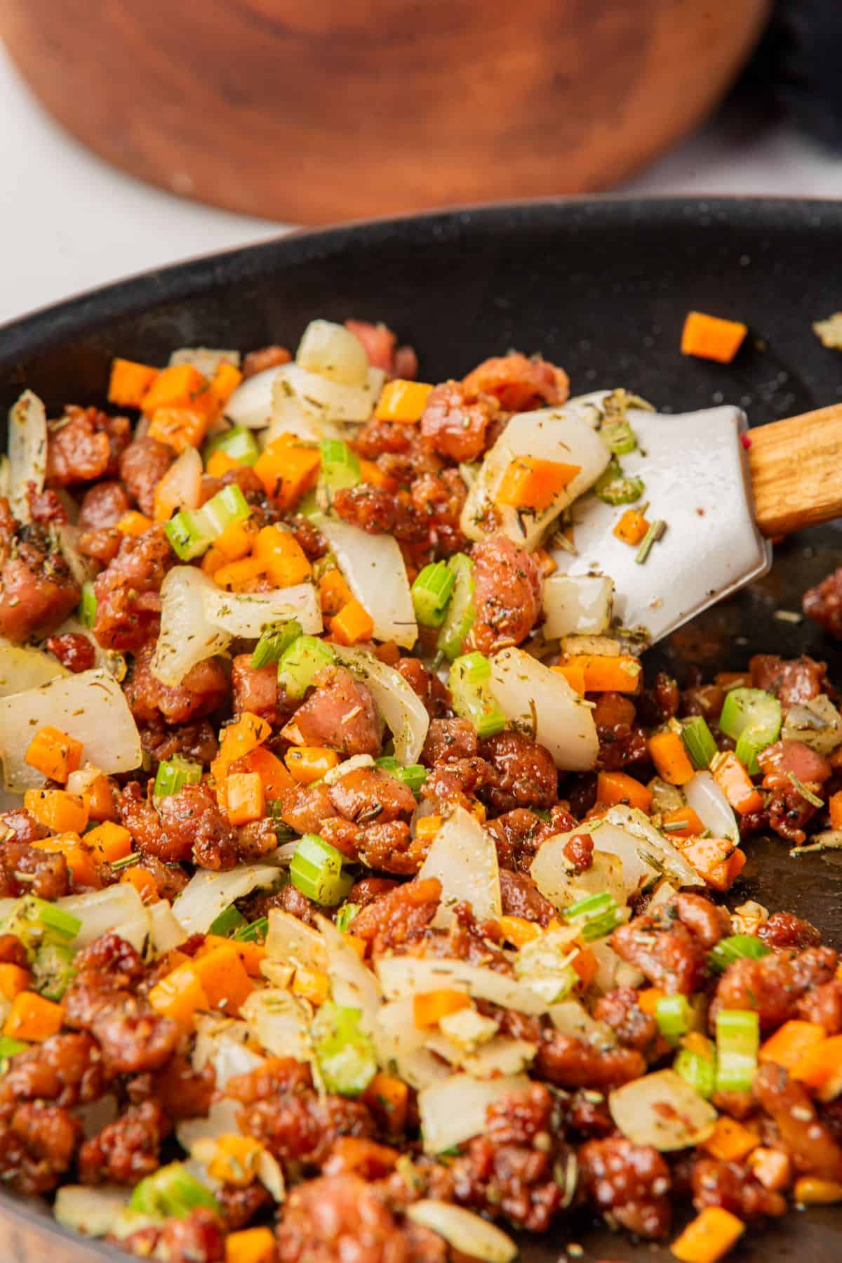 Spatula stirring sautéed vegetables and sausage in a skillet.