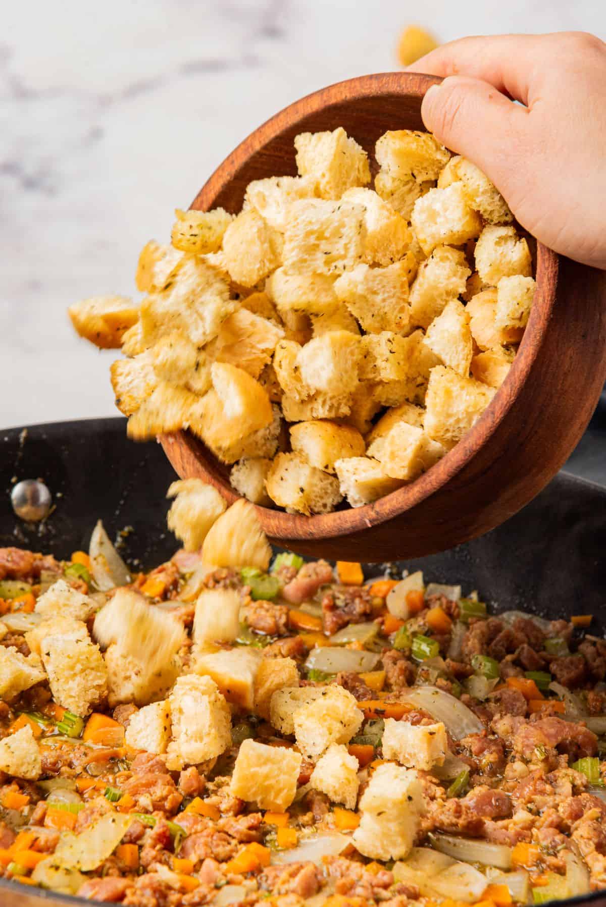 A bowl of Stove Top stuffing mix being poured into a skillet with sausage and veggies. 