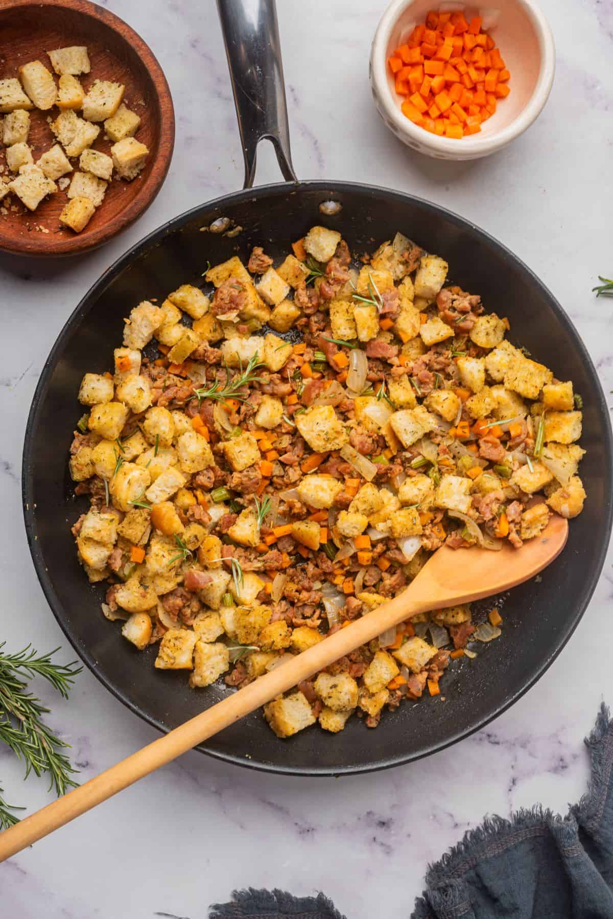 Homemade stovetop sausage stuffing in a skillet with a wooden serving spoon.