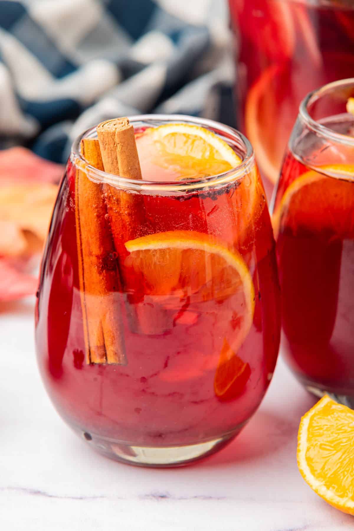 Thanksgiving sangria with red wine in a glass with an orange slice and cinnamon stick garnish.