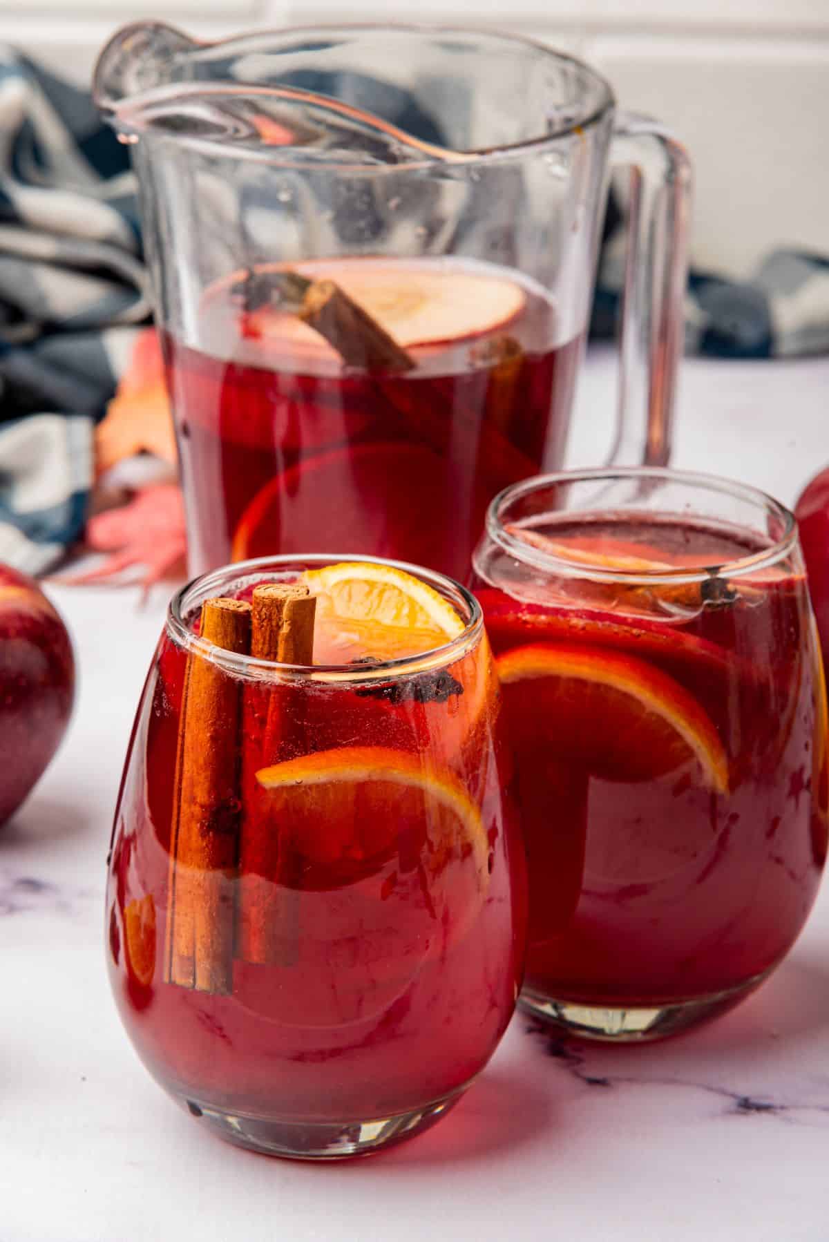 Thanksgiving sangria in a pitcher and two wine glasses with a garnish of cinnamon sticks and orange slices.