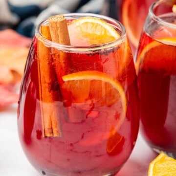 Thanksgiving sangria with red wine in a glass with an orange slice and cinnamon stick garnish.