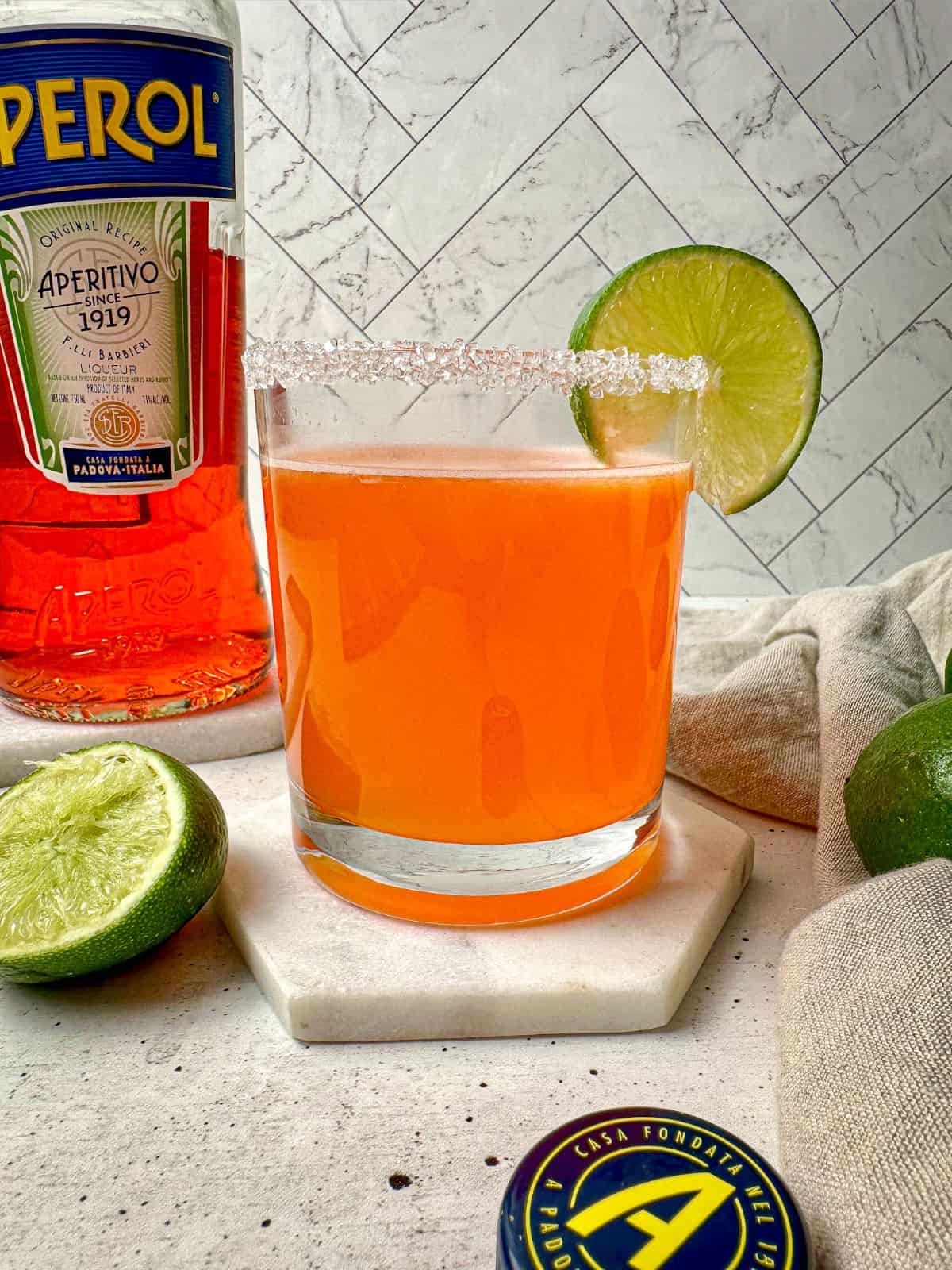 An orange colored Aperol margarita in a rocks glass with a salt rim and lime garnish.