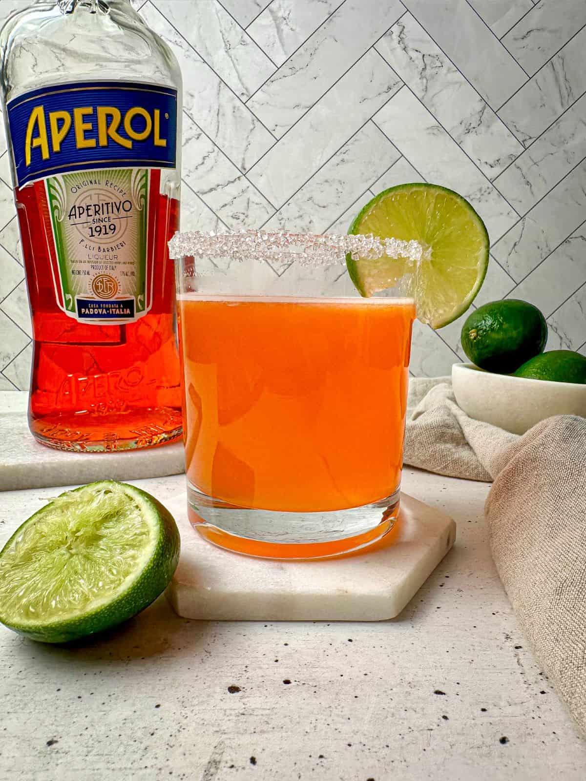 Cocktail with Aperol and tequila in a glass with limes and a bottle of Aperol.