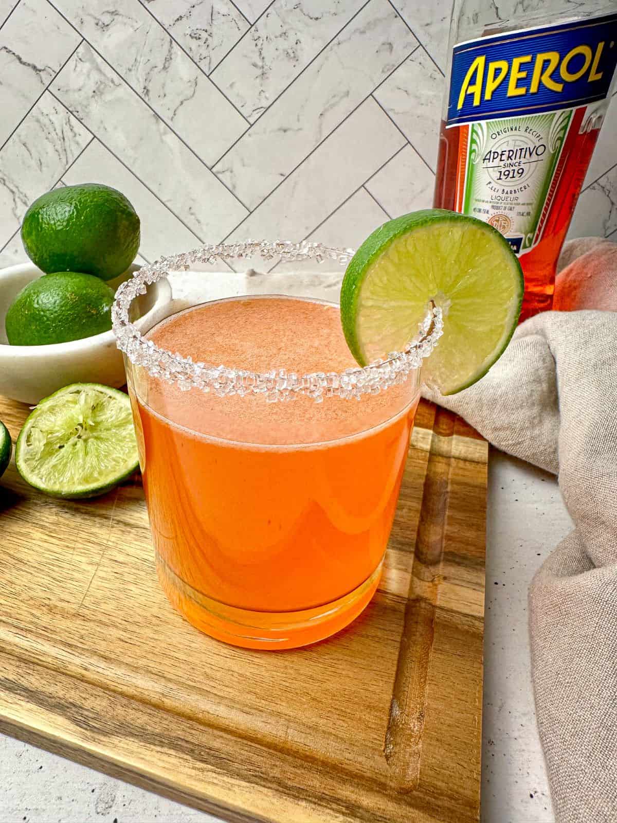 Orange Aperol tequila cocktail in a rocks glass with a salt rim and lime wheel.