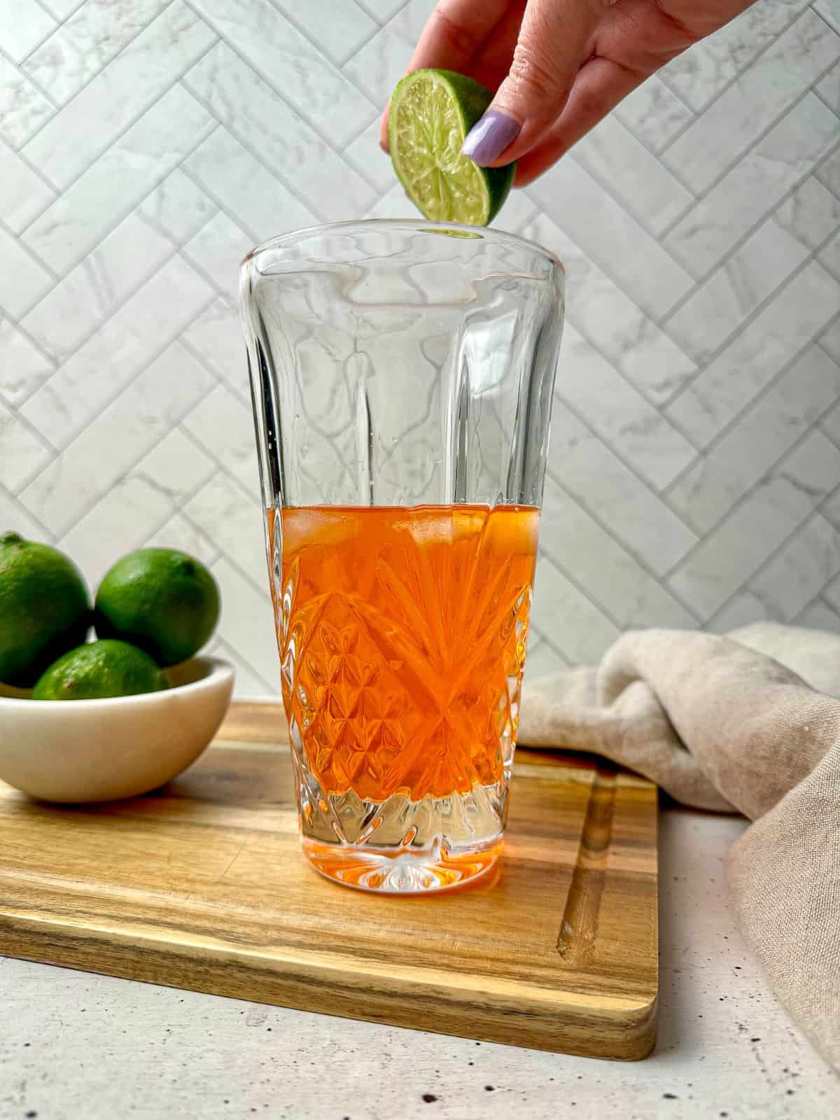 A hand squeezing fresh lime juice in a cocktail shaker with tequila and Aperol.