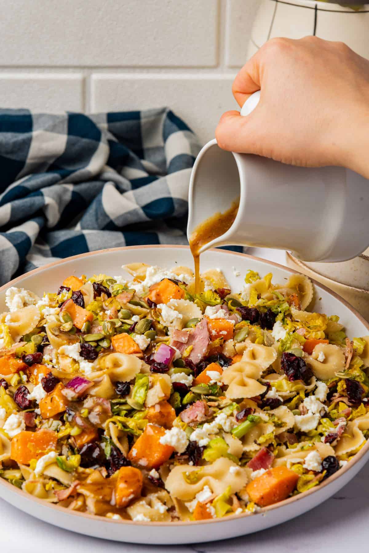 Hand pouring maple balsamic dressing on fall pasta salad with roasted veggies.