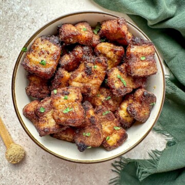 Air fried pork belly bites in a serving bowl with a teaspoon of brown sugar and green towel on the countertop.