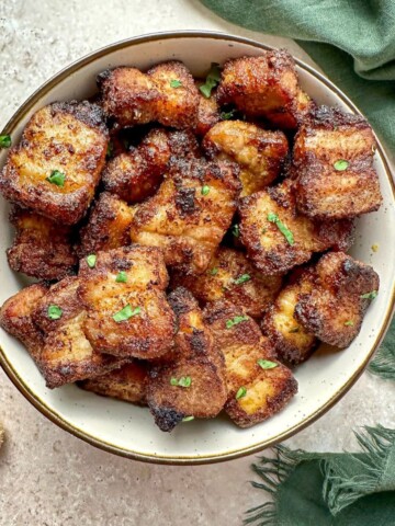 Air fried pork belly bites in a serving bowl with a teaspoon of brown sugar and green towel on the countertop.