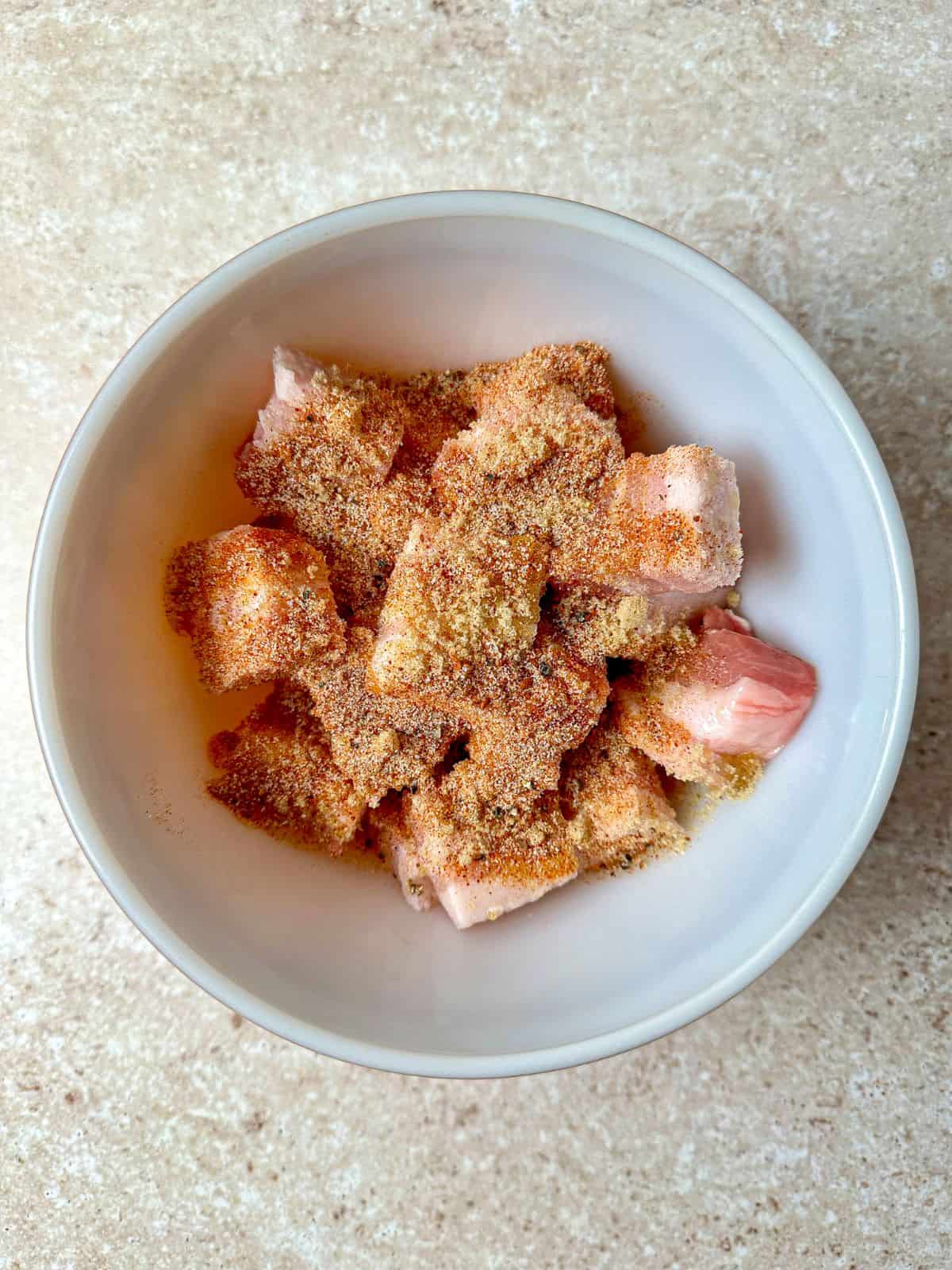 Pork belly bites in a mixing bowl with brown sugar and seasonings.