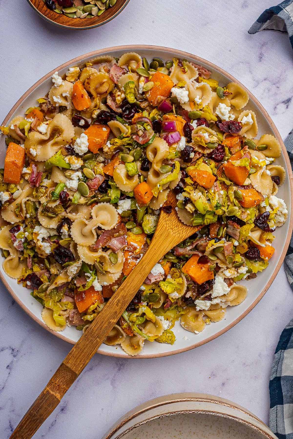 Autumn pasta salad in a large serving bowl with a wooden spoon.