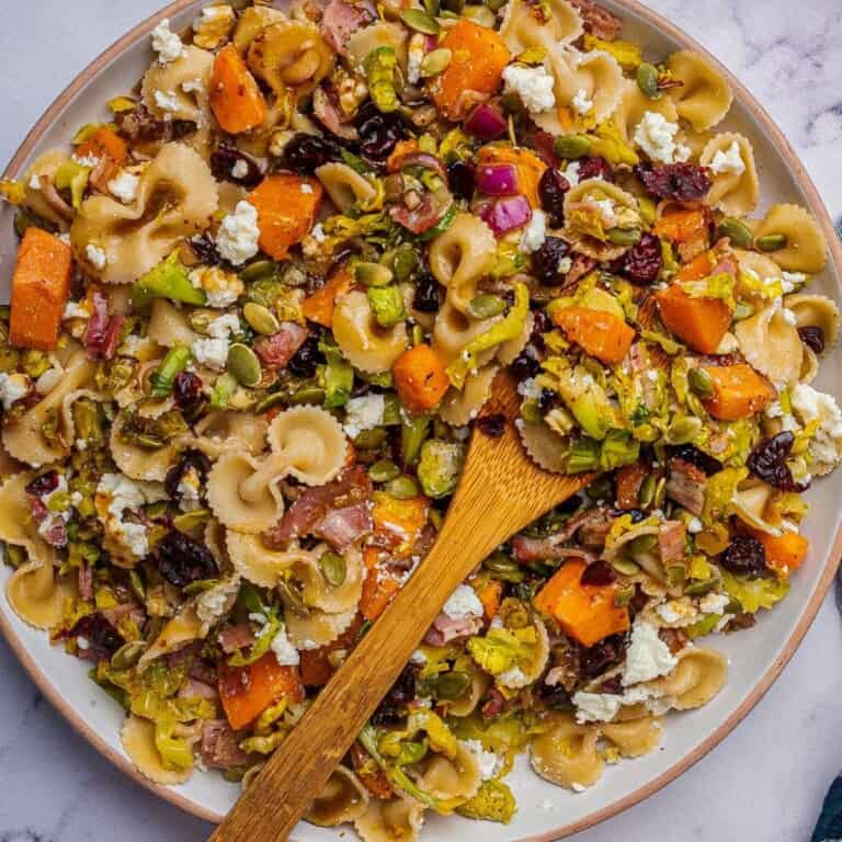 Fall pasta salad with roasted vegetables is in a serving bowl with a wooden spoon.