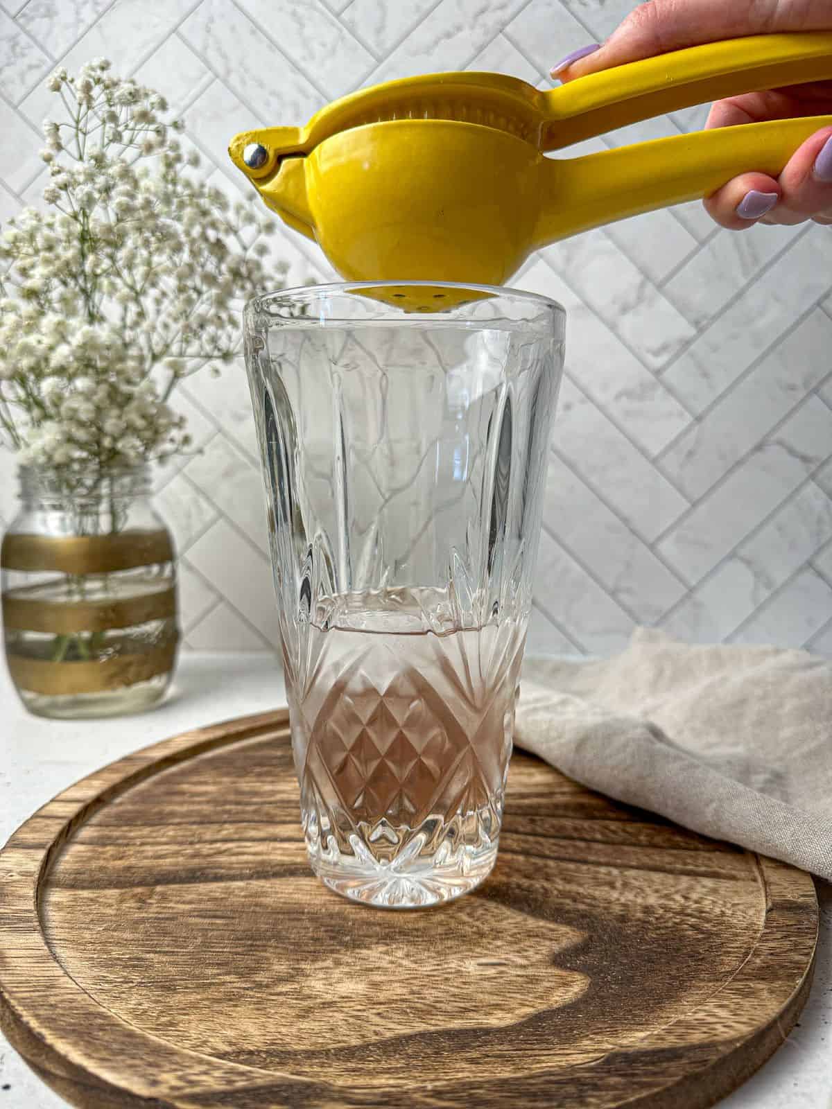 A hand using a citrus squeezer to add fresh lemon juice to a cocktail shaker.