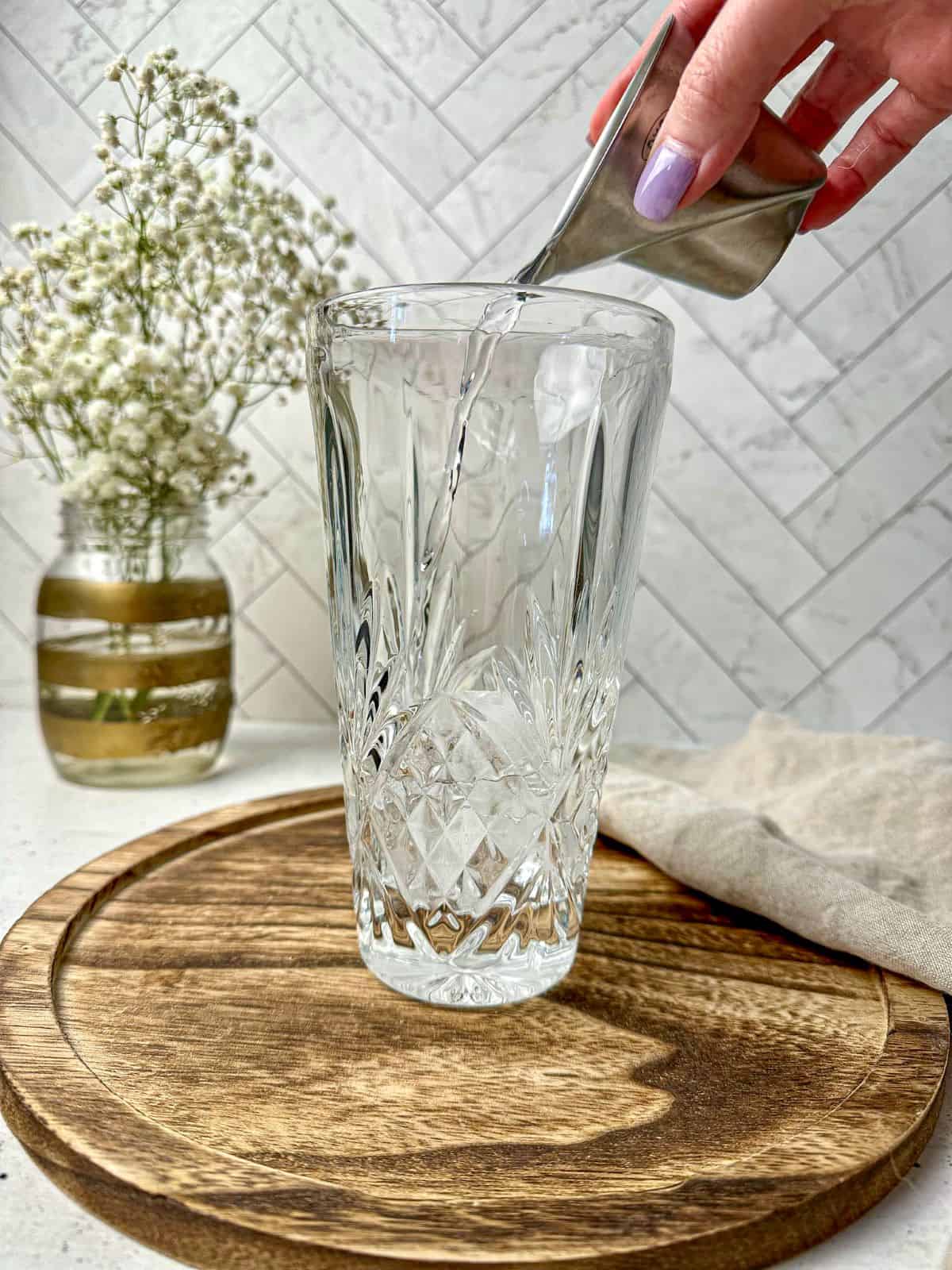 A hand pouring vodka into a cocktail shaker with ice.