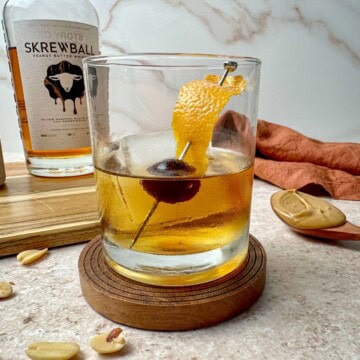 Peanut butter old fashioned cocktail with orange peel and cherry garnish.