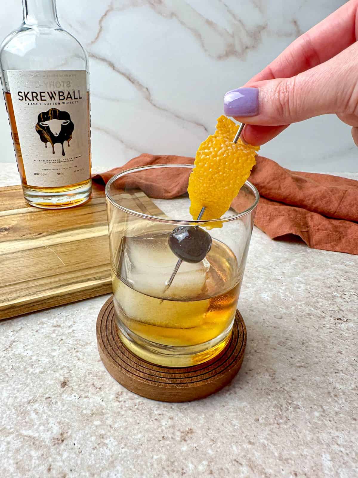 Adding a garnish of an orange peel and cherry to a Skrewball whiskey cocktail.