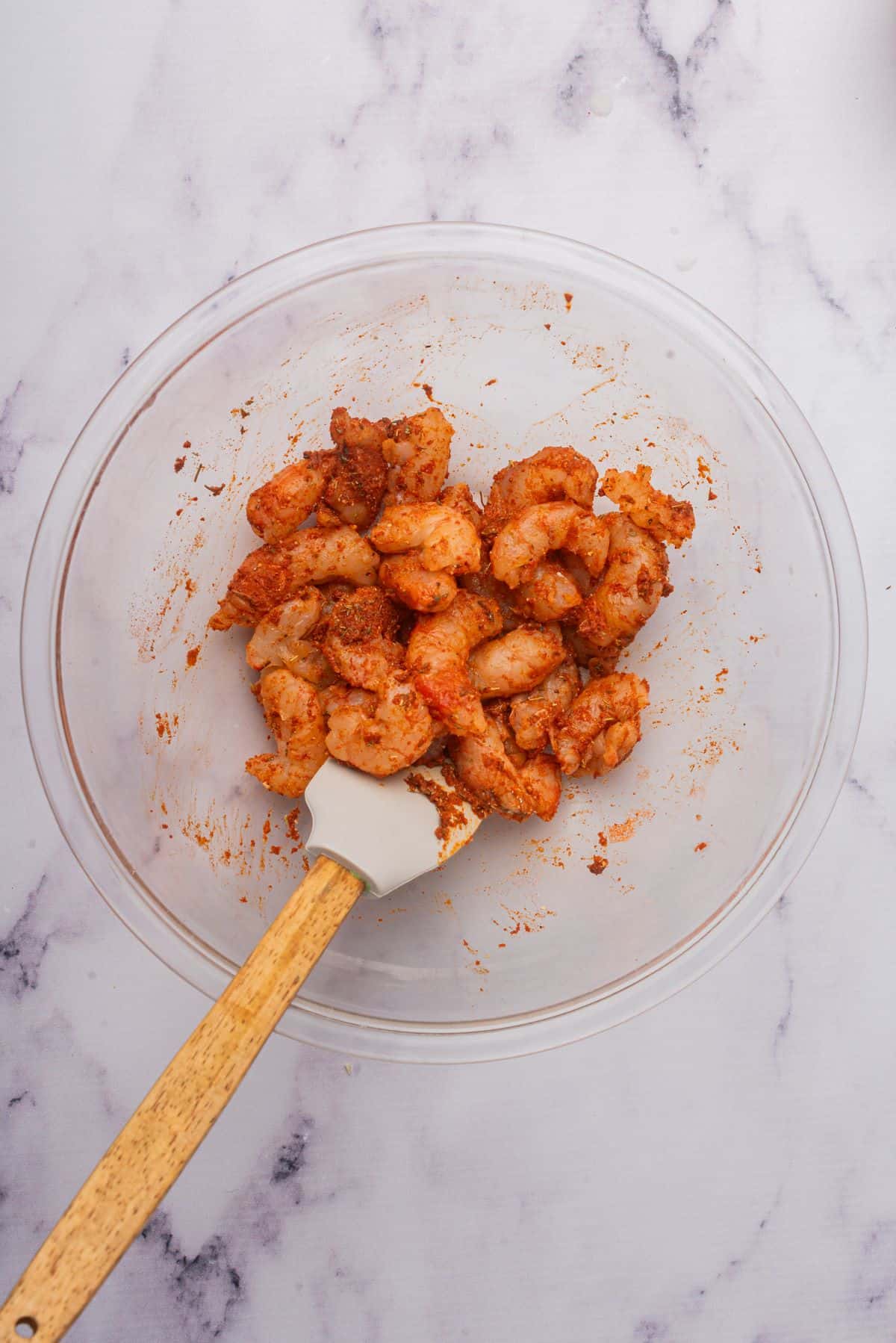 Seasoned Cajun shrimp in a mixing bowl with a spatula.