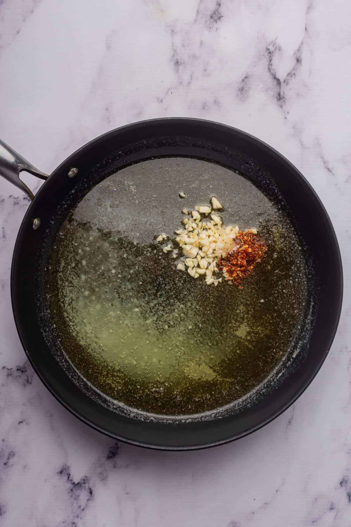 Sautéing butter and olive oil in a skillet with minced garlic and red pepper flakes.