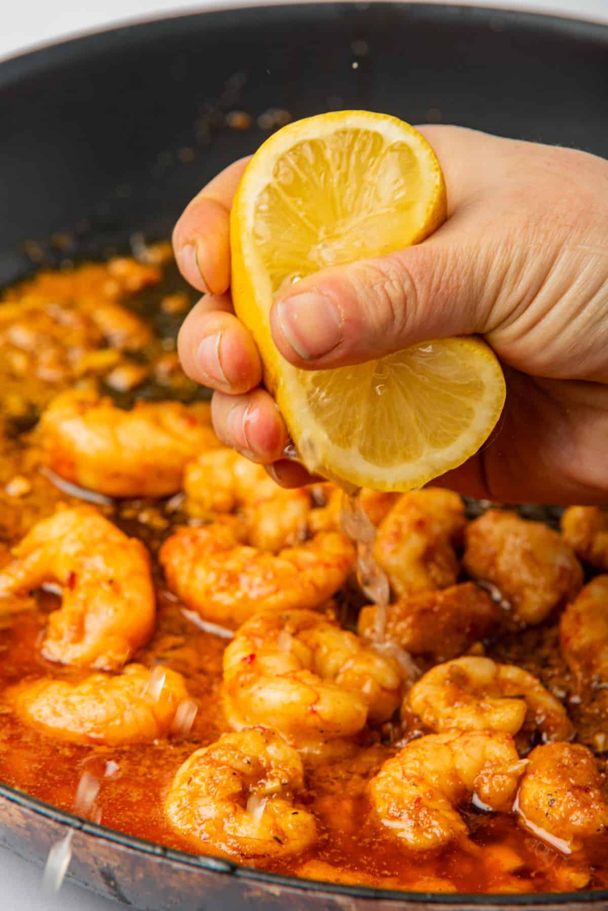 A hand squeezing a lemon into the Cajun shrimp scampi recipe.